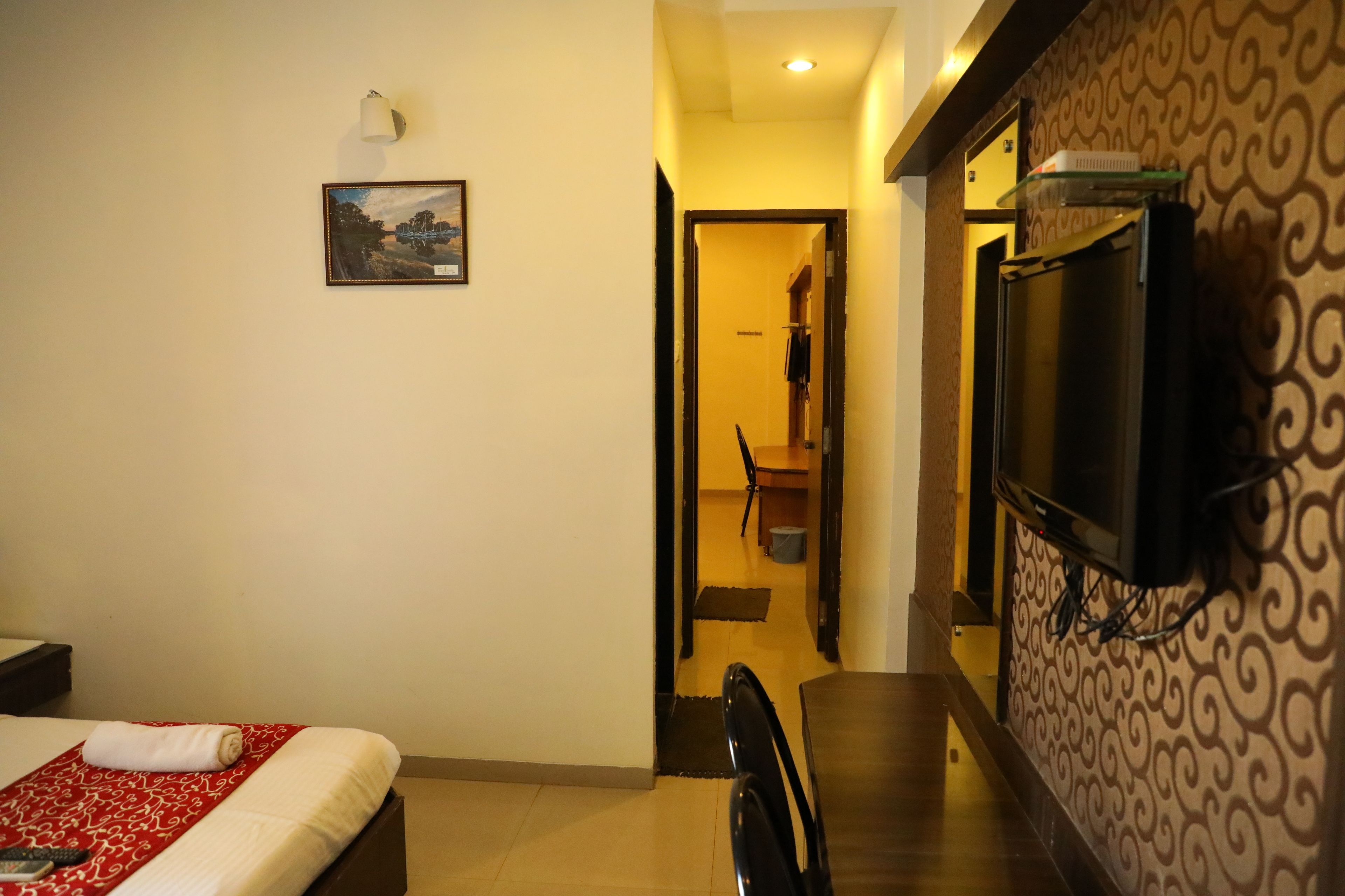 Habitación de hotel con cama, televisor montado en la pared y pasillo que conduce a un baño.