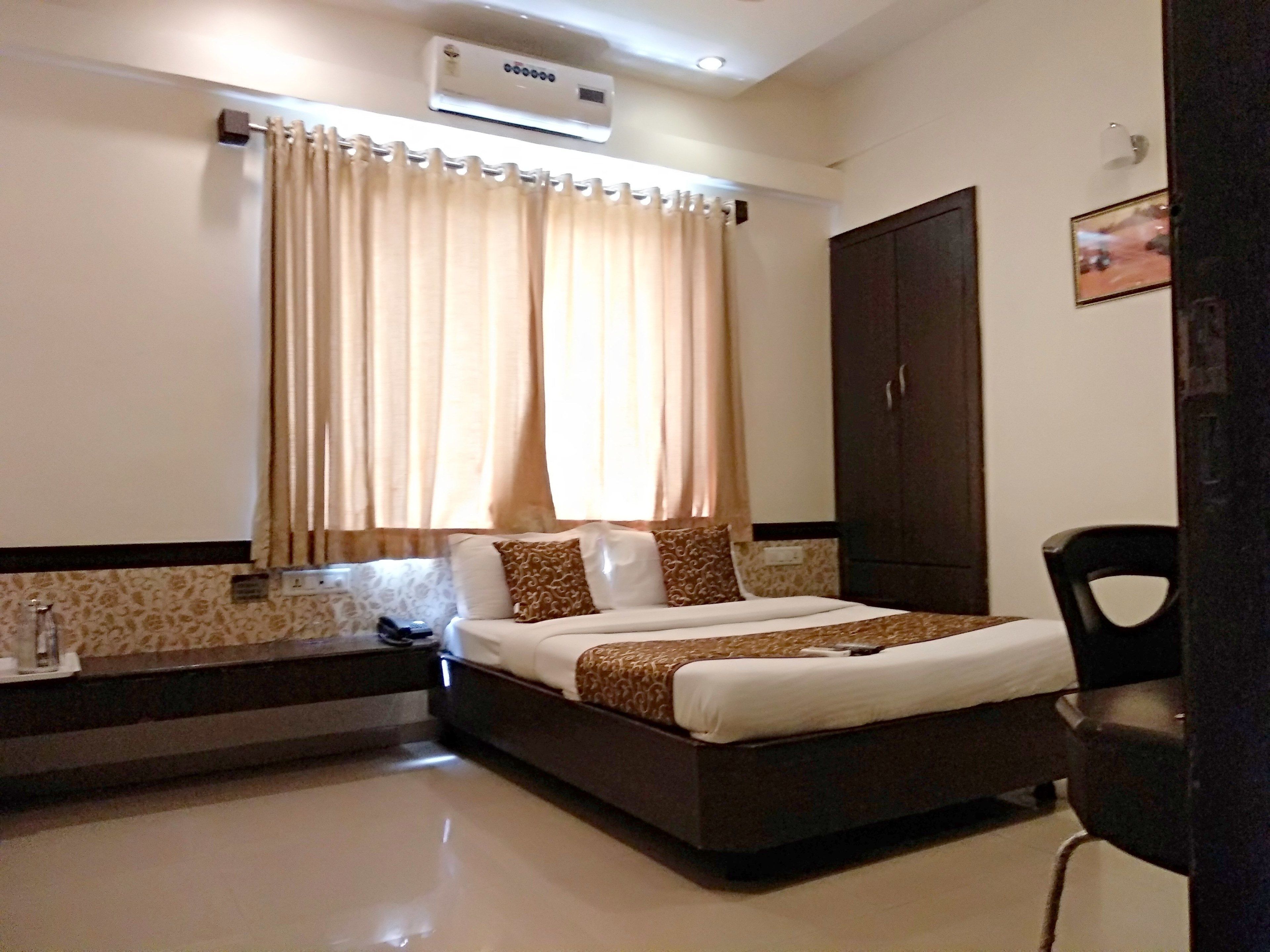 A hotel room with a bed, a wardrobe, a desk with a chair, and a window with curtains.