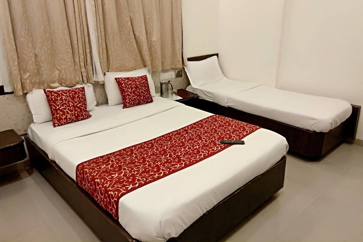 A hotel room with a large bed, a smaller single bed, and a bedside table with a lamp.