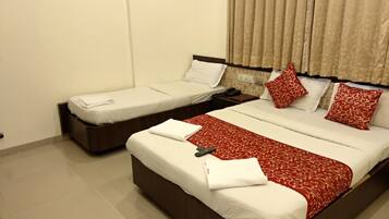 Habitación de hotel con dos camas individuales y una cama doble. Cada cama tiene sábanas blancas y colchas estampadas de rojo. Junto a la cama doble hay una mesita de noche con un teléfono y un libro. El piso es de baldosas y las cortinas de la ventana son color beige.