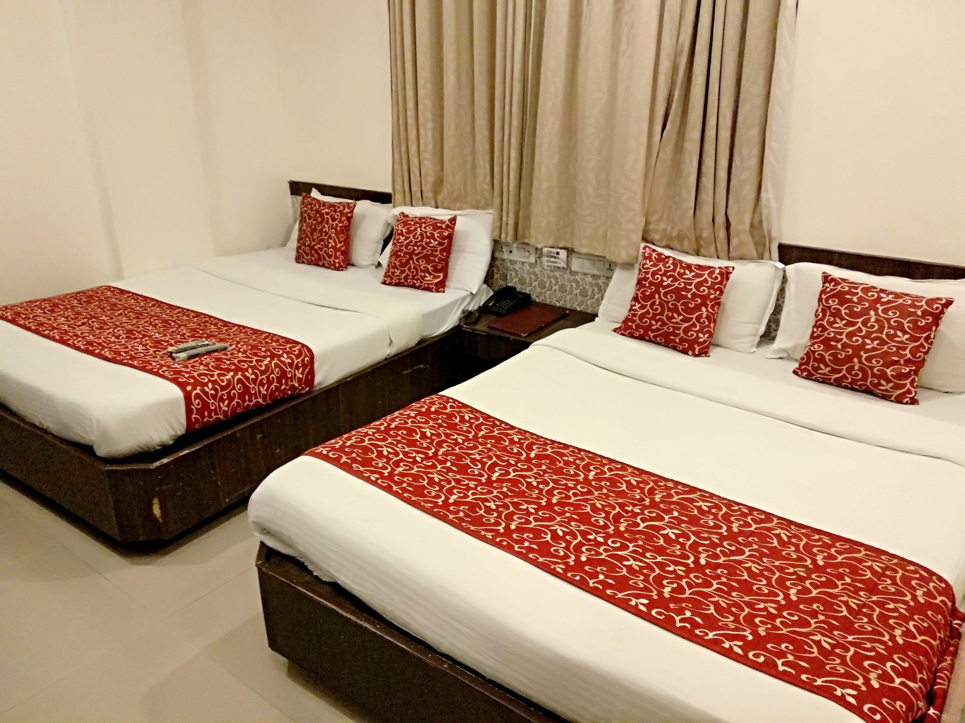 Dos camas individuales con ropa de cama roja y blanca, un cabecero de madera, una mesita de noche con un teléfono y cortinas color beige.