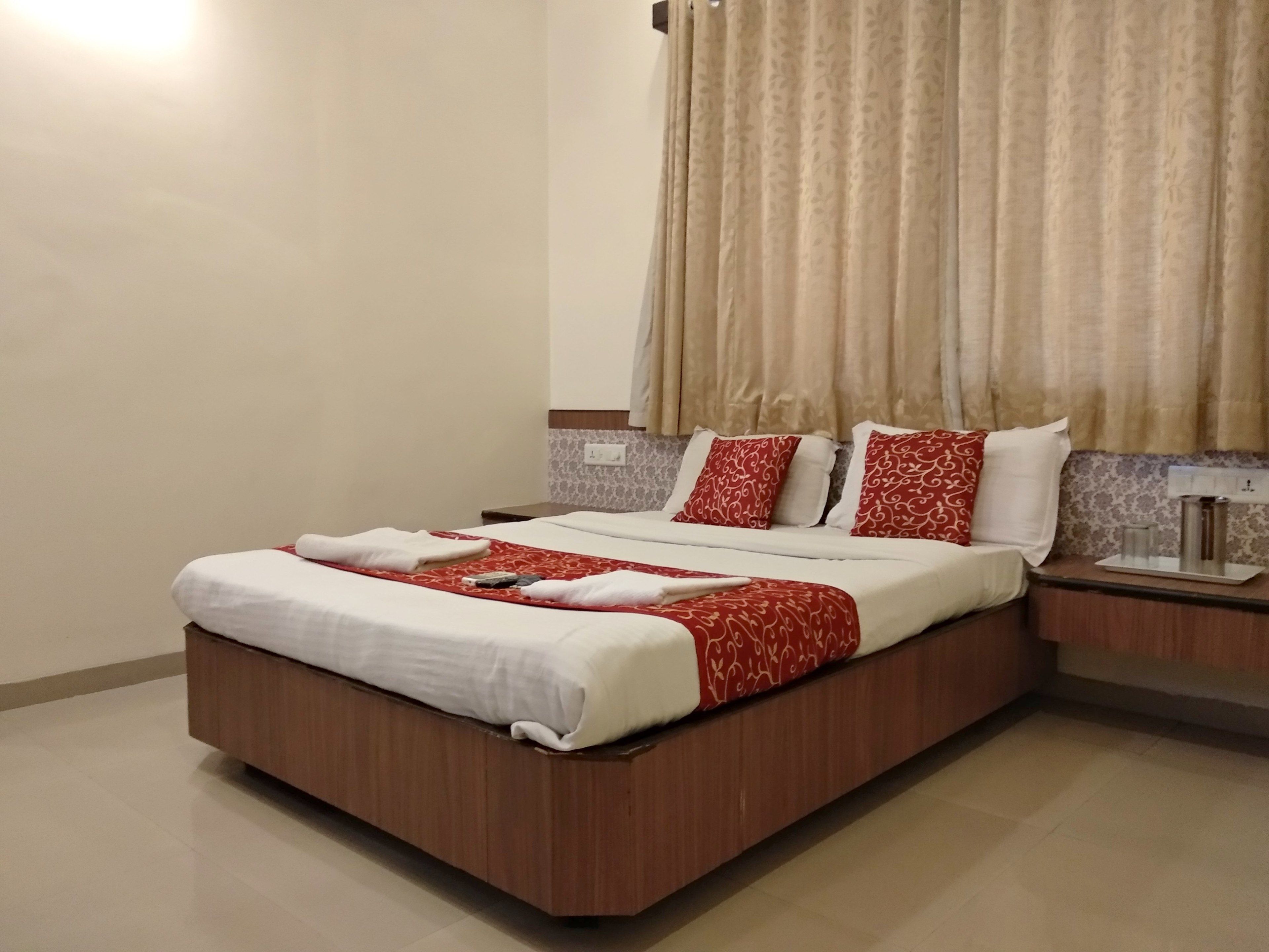 A neatly made bed with a red and white patterned bedspread, two pillows with red and white patterns, and a bedside table with a lamp and a glass.
