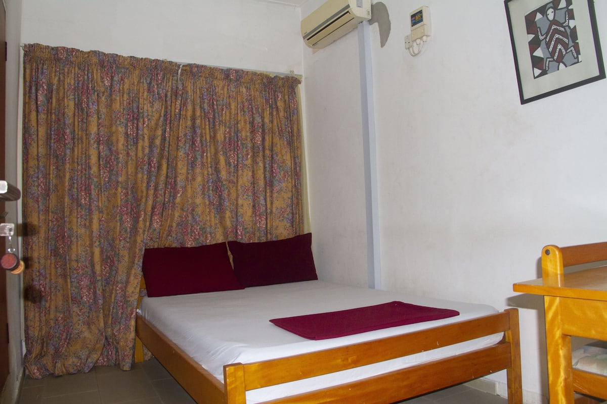 Uma cama de solteiro com estrutura de madeira, um travesseiro vermelho e um cobertor roxo.