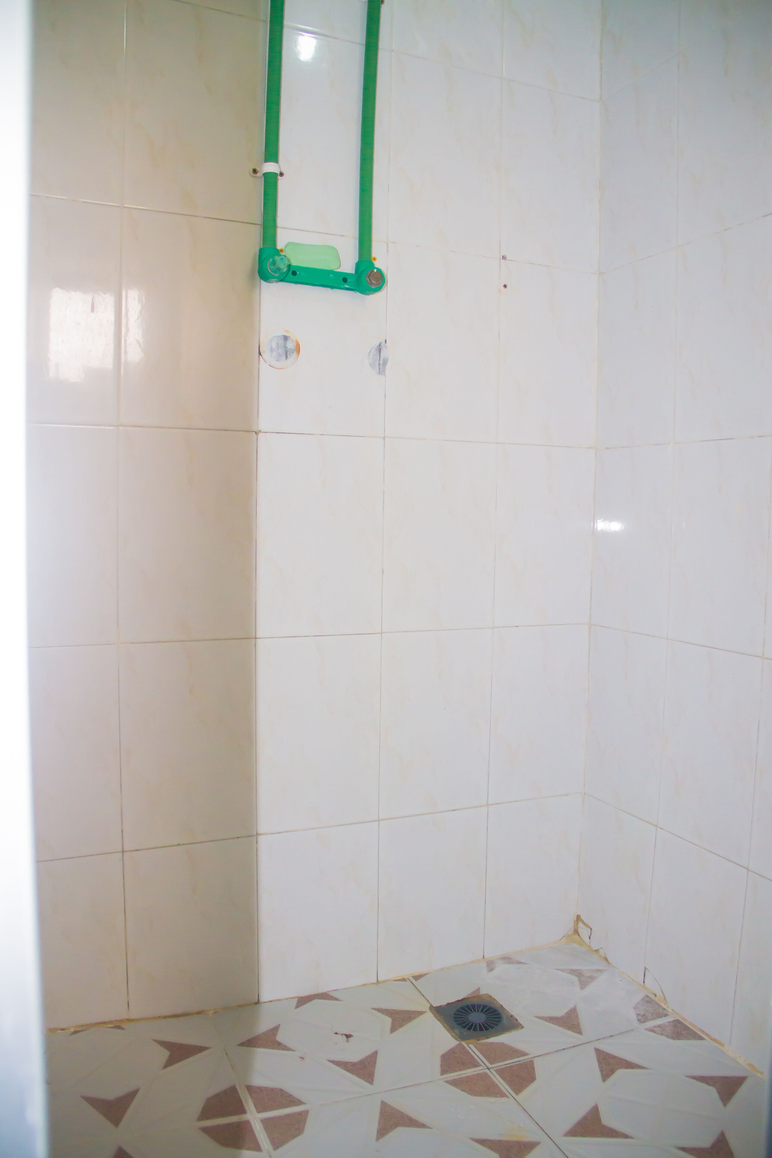 Un baño pequeño con azulejos, una zona de ducha, un perchero verde y un desagüe en el suelo.