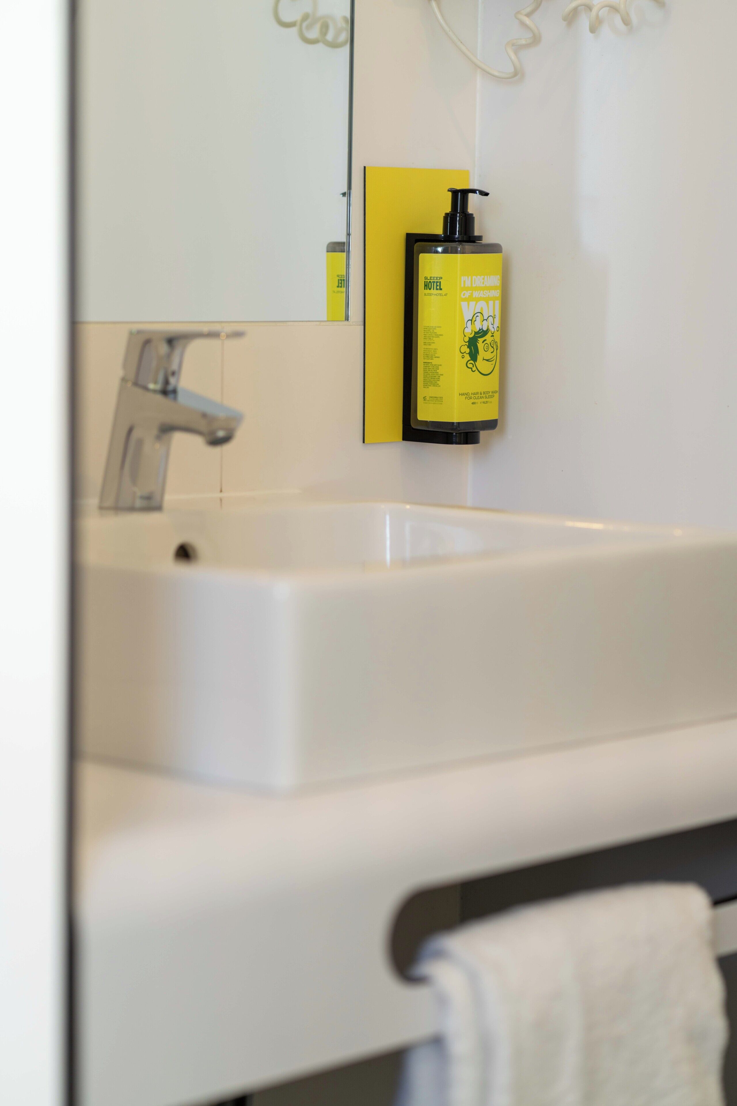 A bathroom with a white sink, a yellow bottle of hotel shampoo, and a white towel.