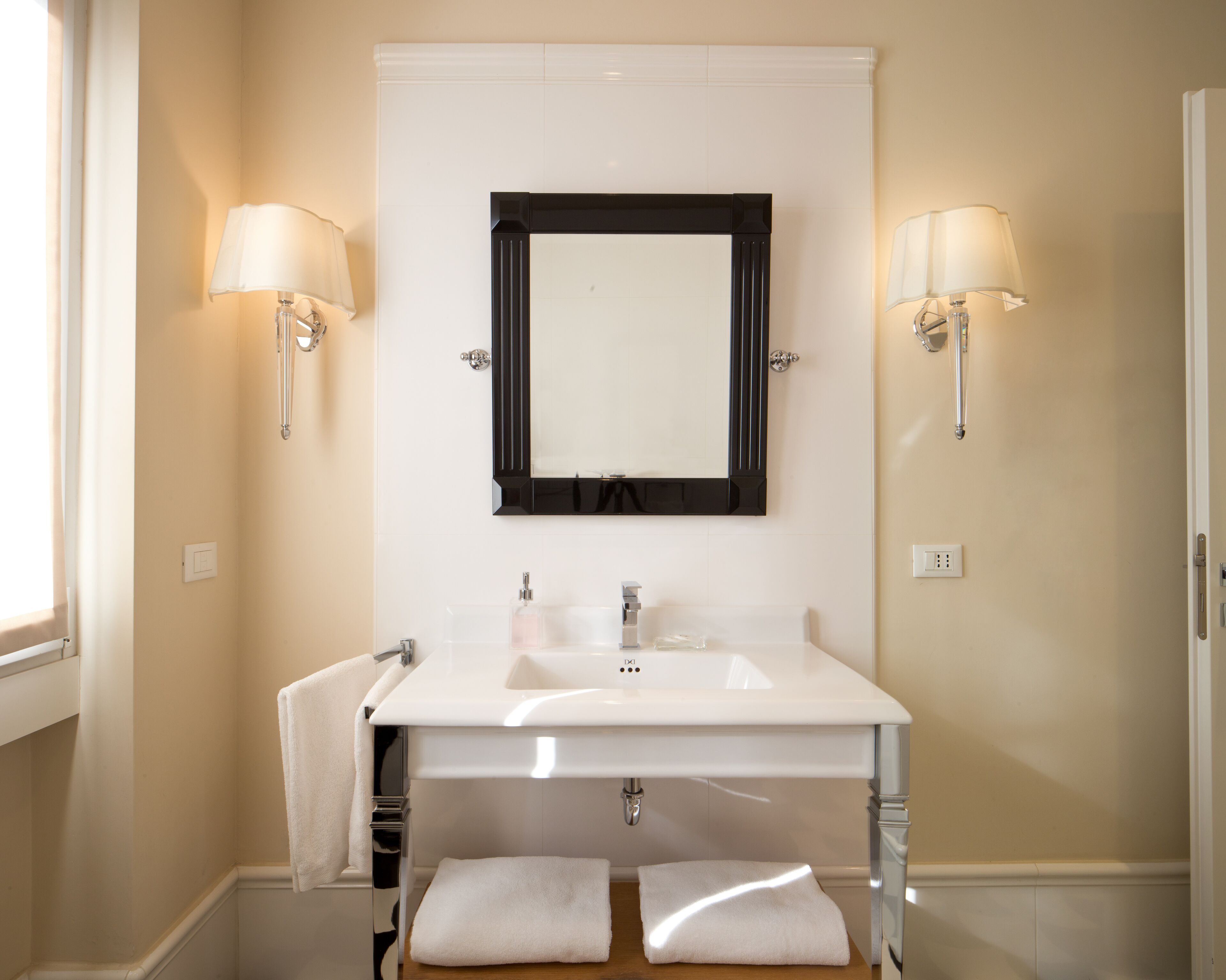 Une salle de bain avec un lavabo blanc, un miroir et deux appliques murales.