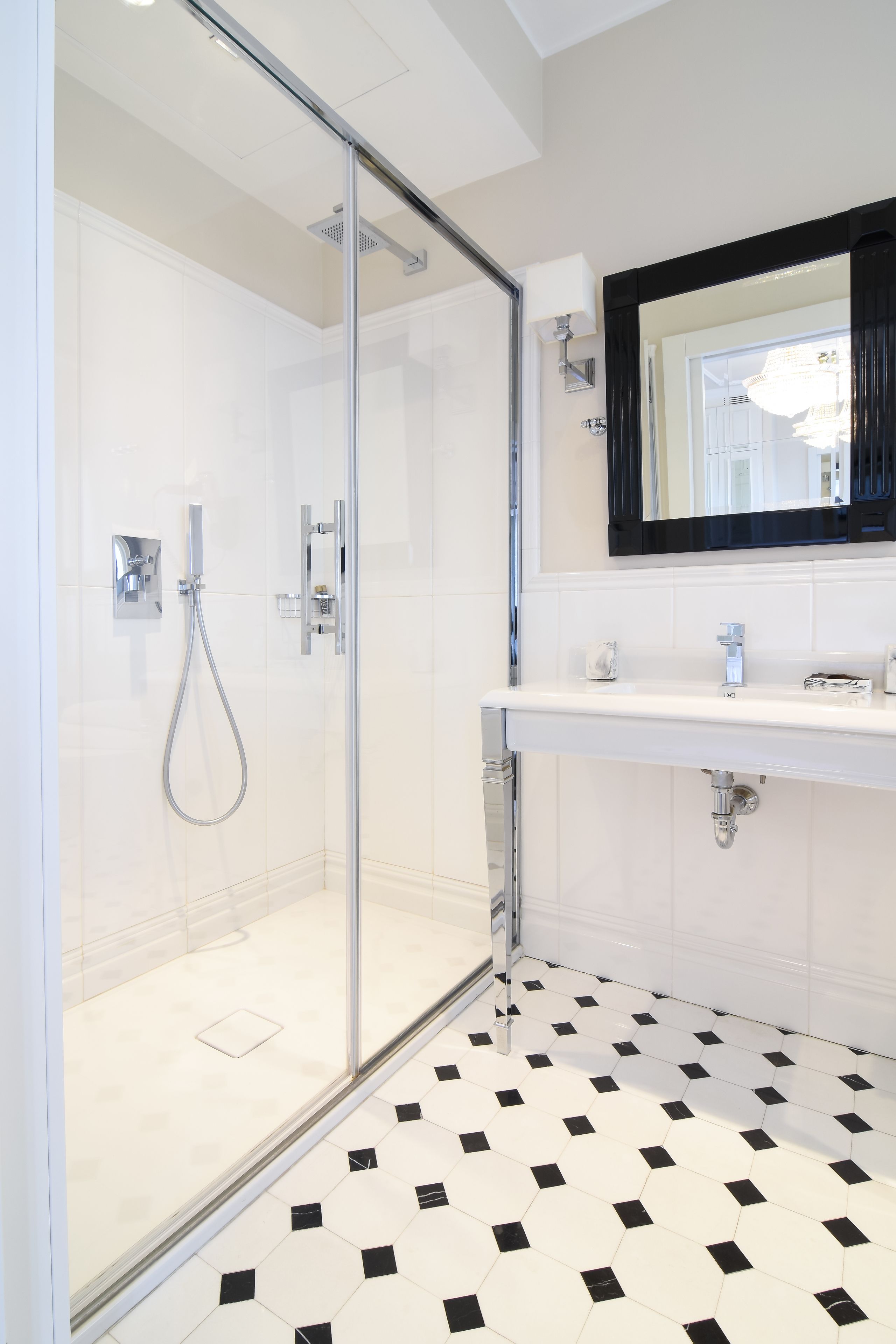 Une salle de bain moderne avec une douche à parois de verre, un lavabo blanc et un sol carrelé en noir et blanc.