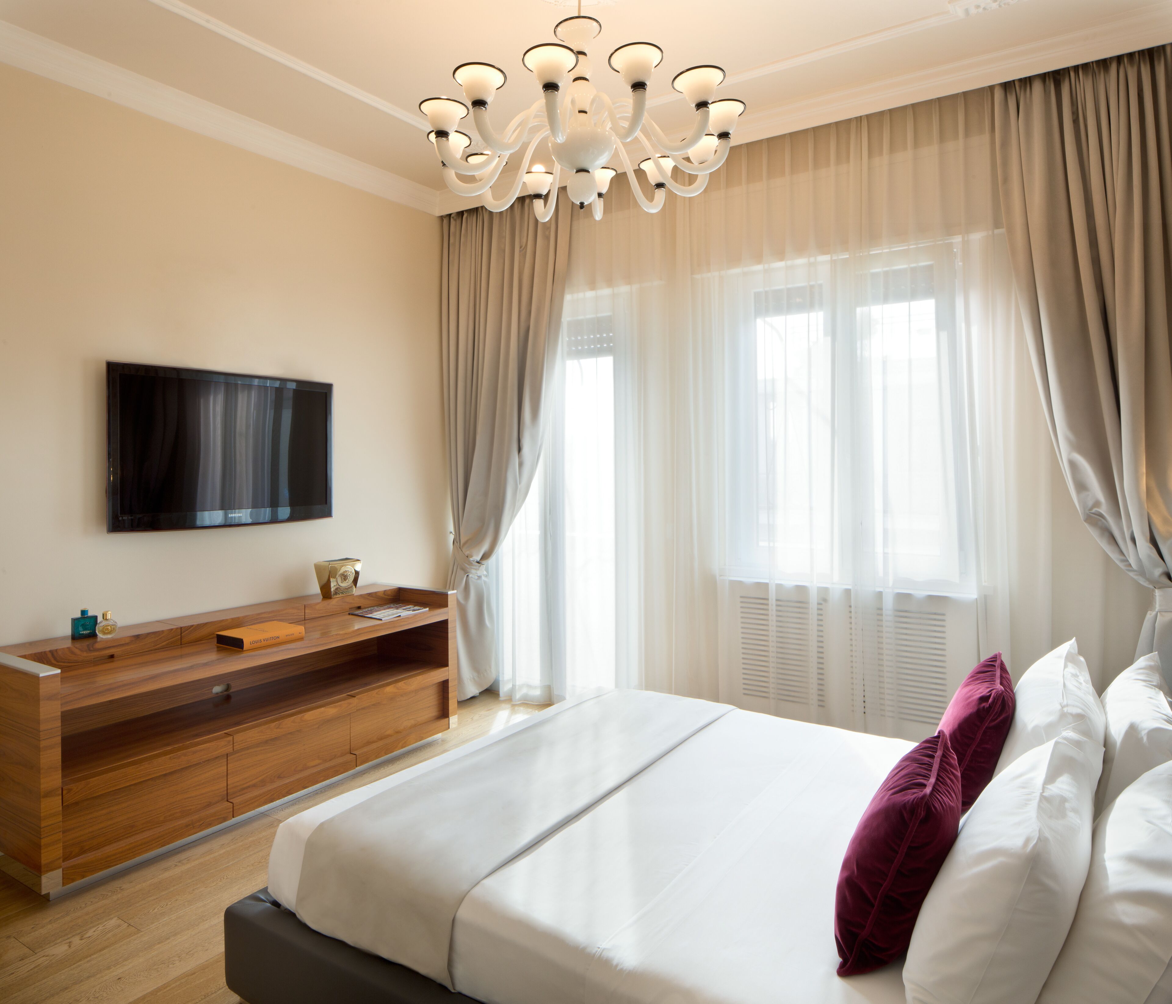 A modern hotel room with a large bed, a wooden dresser, a flat-screen TV, and a large window with curtains.