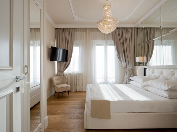 Un dormitorio de hotel con una cama grande, un televisor montado en la pared, una silla y una araña.
