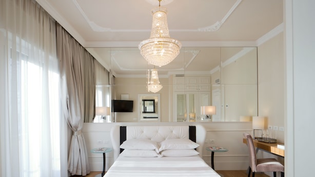 A hotel room with a large bed, a desk, a chair, a television, and a chandelier. - Luxury Suite Milano Duomo (Milan)