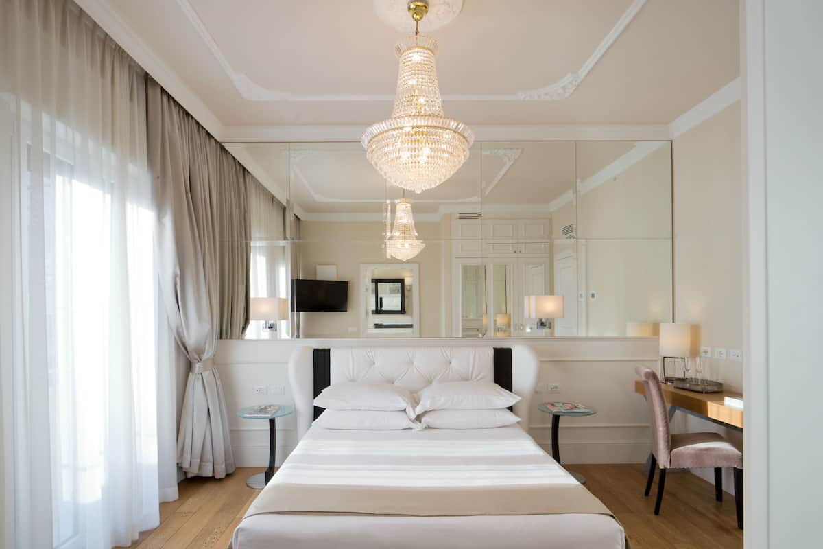 Ein Hotelzimmer mit einem großen Bett, einem Schreibtisch, einem Sessel, einem Fernseher und einer Kristallleuchter.