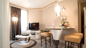 A modern hotel room with a dining area, a flat-screen TV, a small table with a vase of flowers, and a bar area with stools. - Luxury Suite Milano Duomo (Milan)
