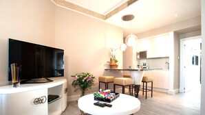 A modern living room with a flat-screen TV, a white entertainment unit, a round coffee table, and a kitchen area with a dining table and bar stools. - Luxury Suite Milano Duomo (Milan)
