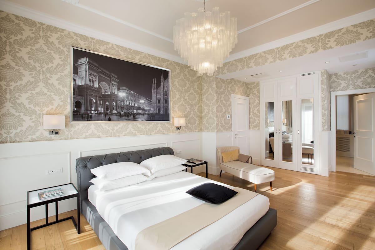 Ein modernes Schlafzimmer mit einem großen Bett, einer Chandelüstere, einem Poster mit Stadtansicht und einem begehbaren Kleiderschrank.