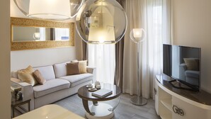 A modern hotel room with a sofa, a round coffee table with a book and teapot, a TV on a cabinet, and a large mirror with a decorative frame. - Luxury Suite Milano Duomo (Milan)