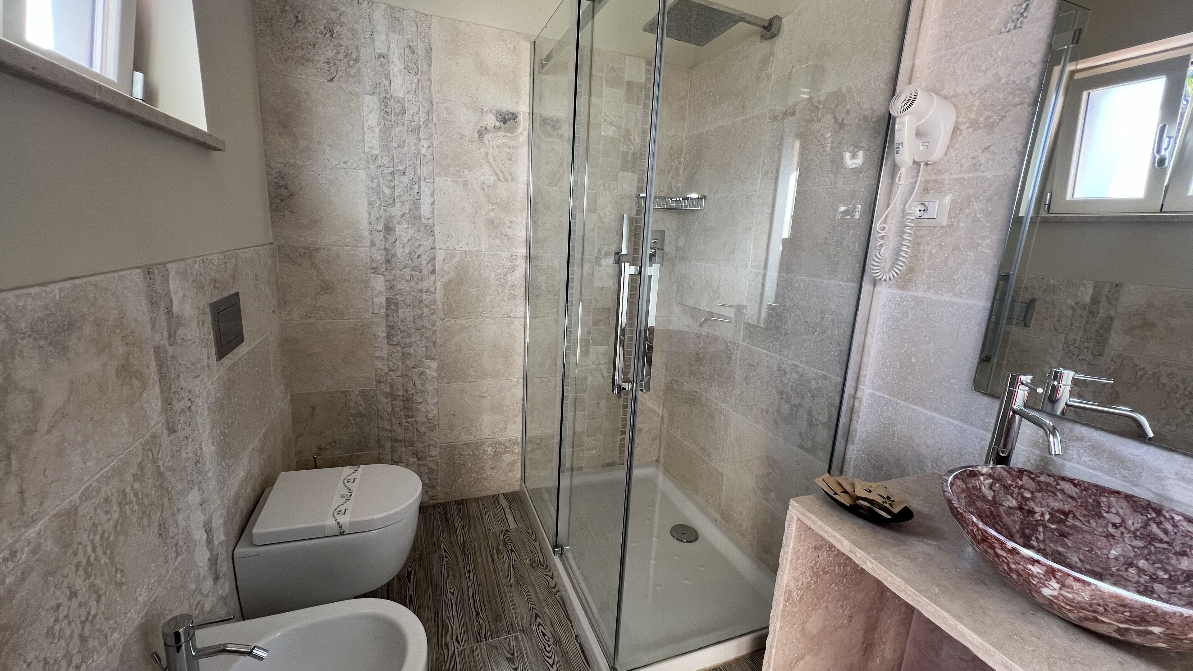 A modern bathroom with a glass shower enclosure, a white toilet, a bathtub, and a marble sink with a mirror.