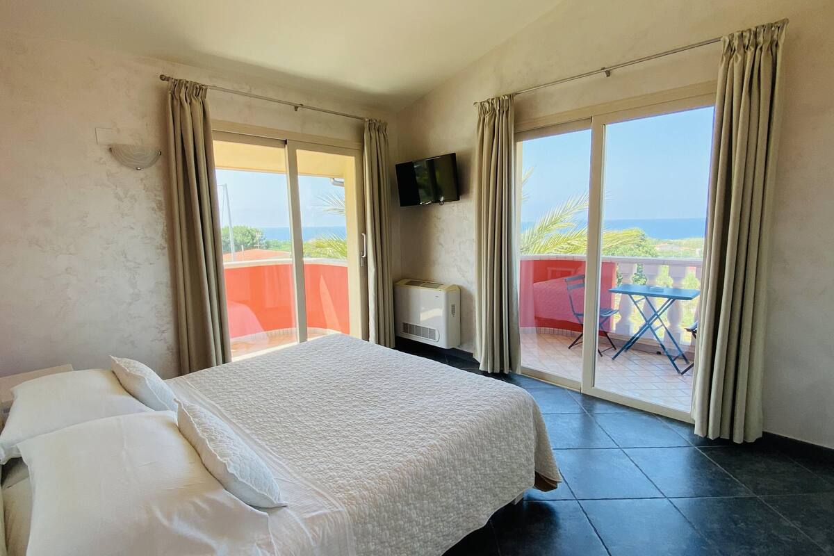 A hotel room with a bed, a TV, and a balcony with a table and chairs.