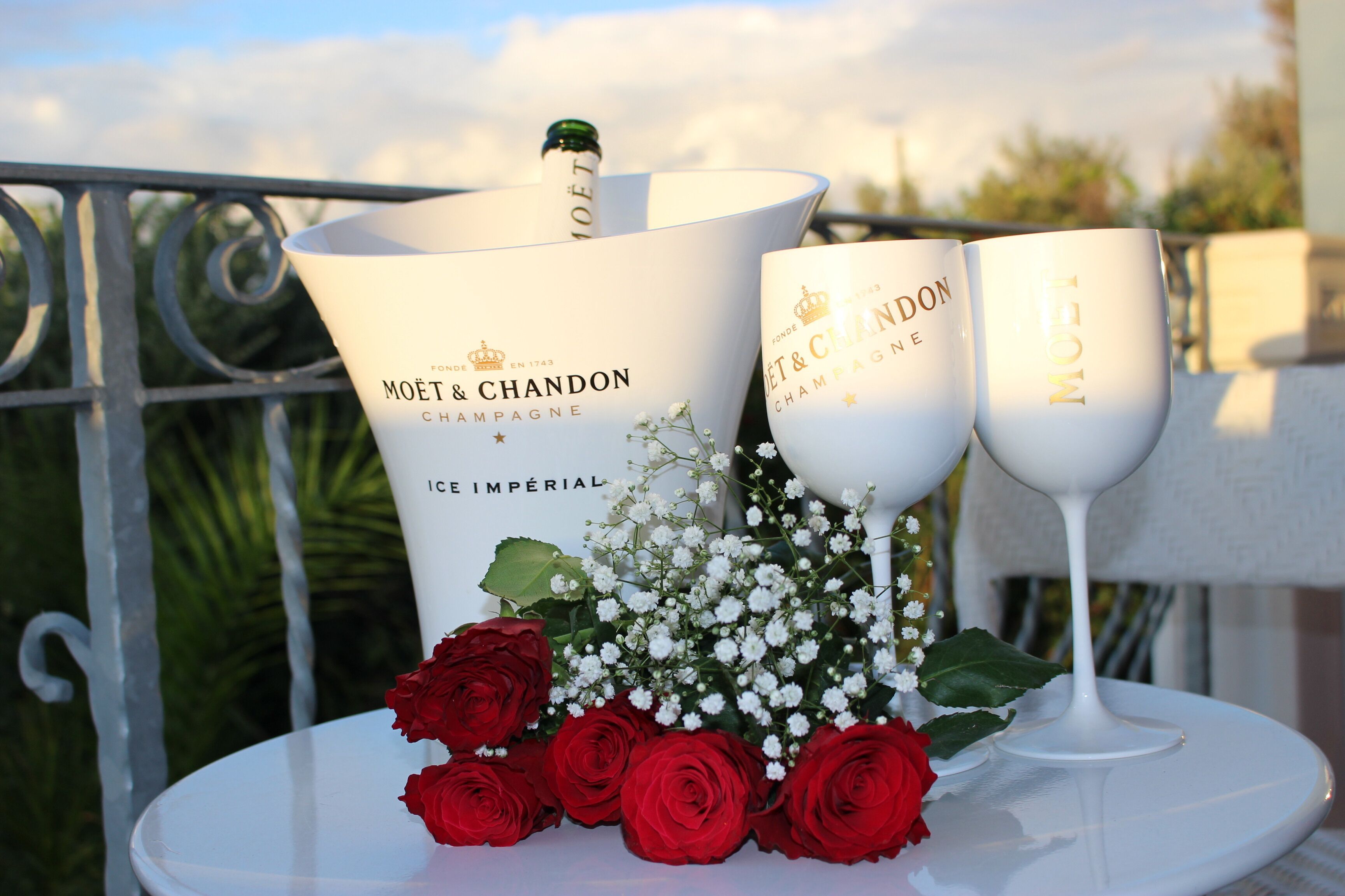 Una mesa con dos copas de champán Moët & Chandon, una botella grande y rosas rojas.