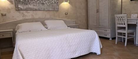 A bedroom with a bed, a desk, a chair, a wardrobe, and a painting on the wall.