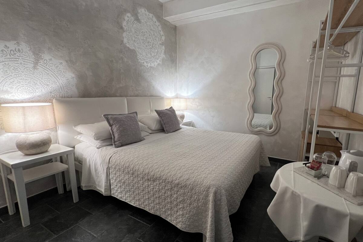 A bedroom with a large bed, bedside tables, a mirror, and a small table with toiletries.