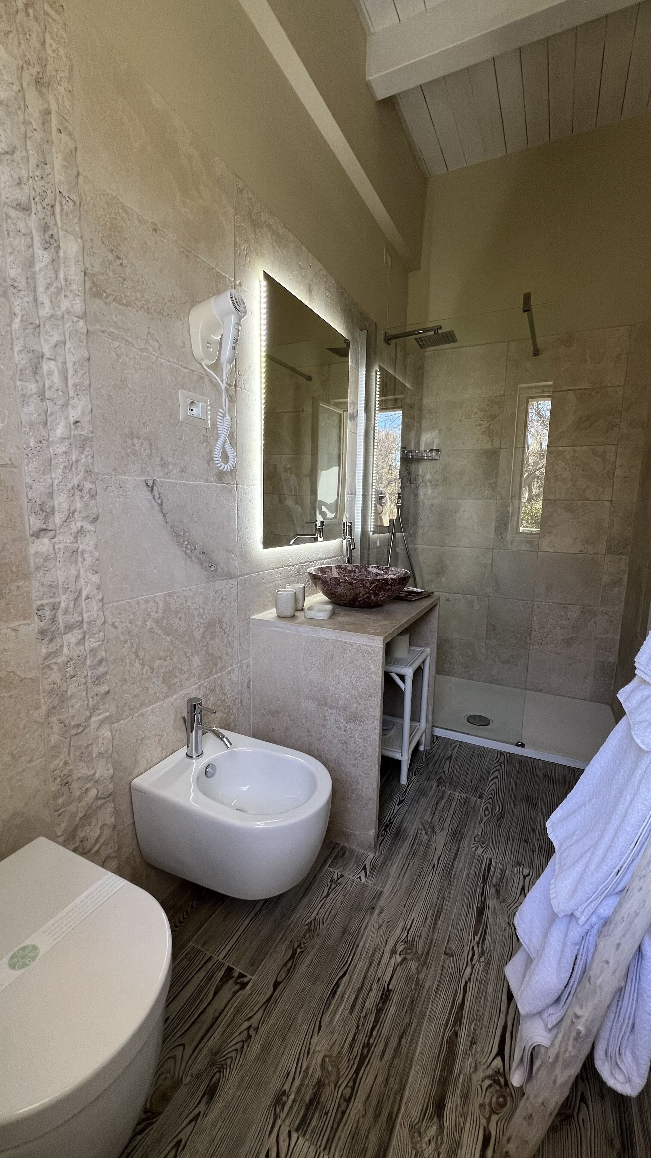 A bathroom with a large sink, a mirror, a shower, and a towel rack.