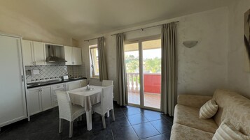 Cocina compacta con armarios blancos, una mesa de comedor con sillas y un balcón con barandilla roja.