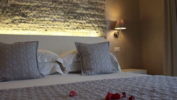 A neatly made bed with a textured blanket and two pillows, a stone wall with a light fixture above it, and a wall-mounted lamp to the right.