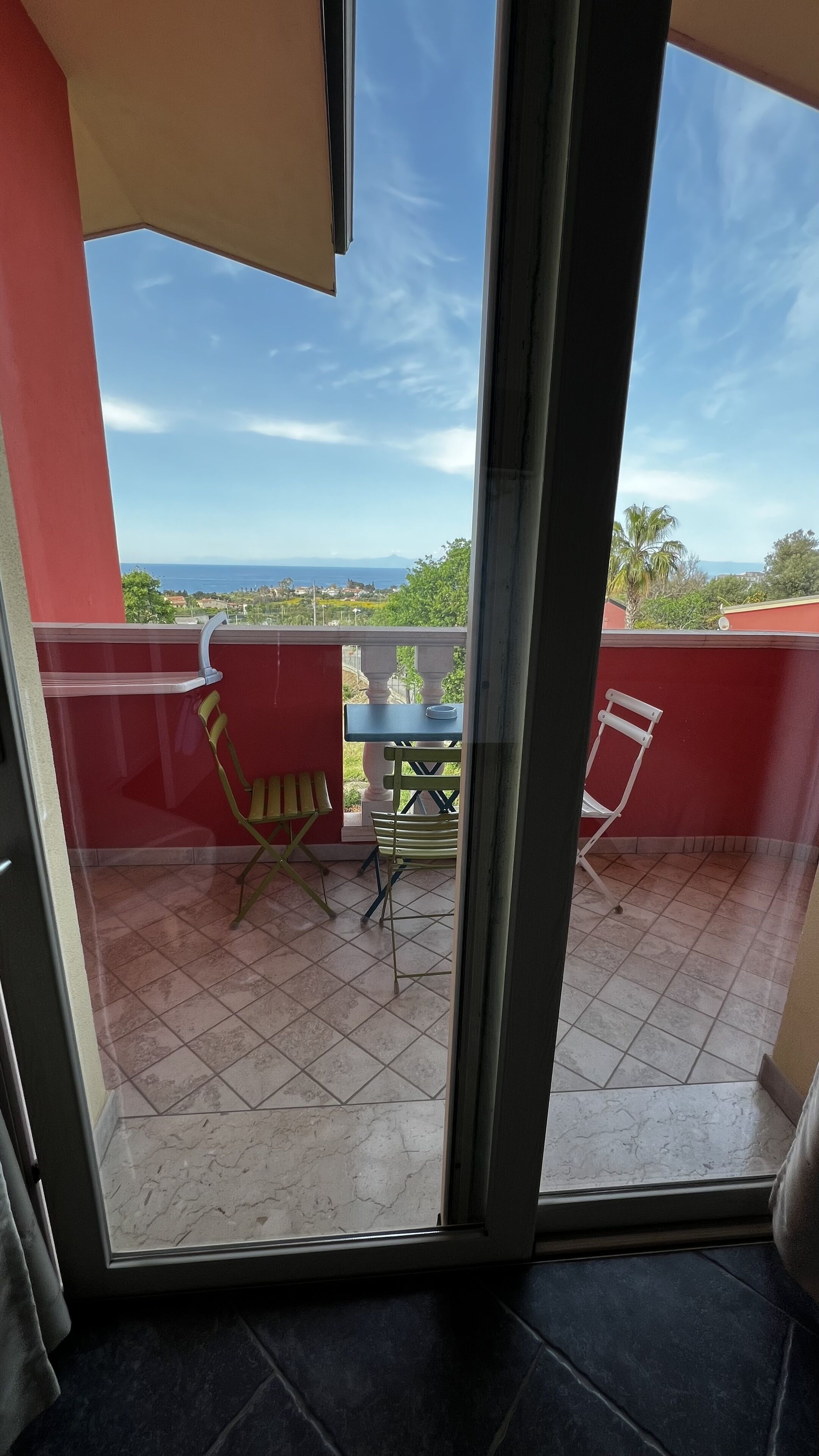 A balcony with a table and chairs, a view of the sea, and a red wall.