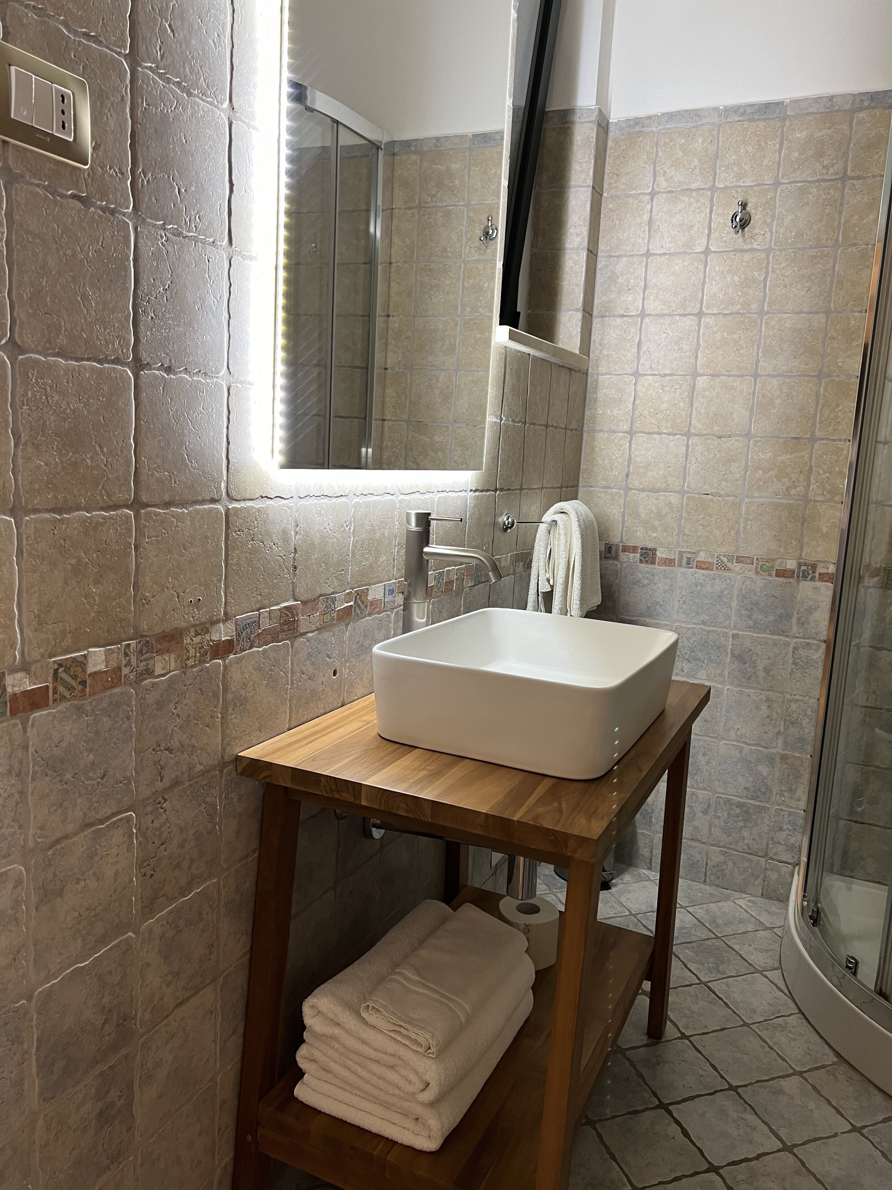 A bathroom with a white sink, wooden vanity, and a glass shower enclosure.