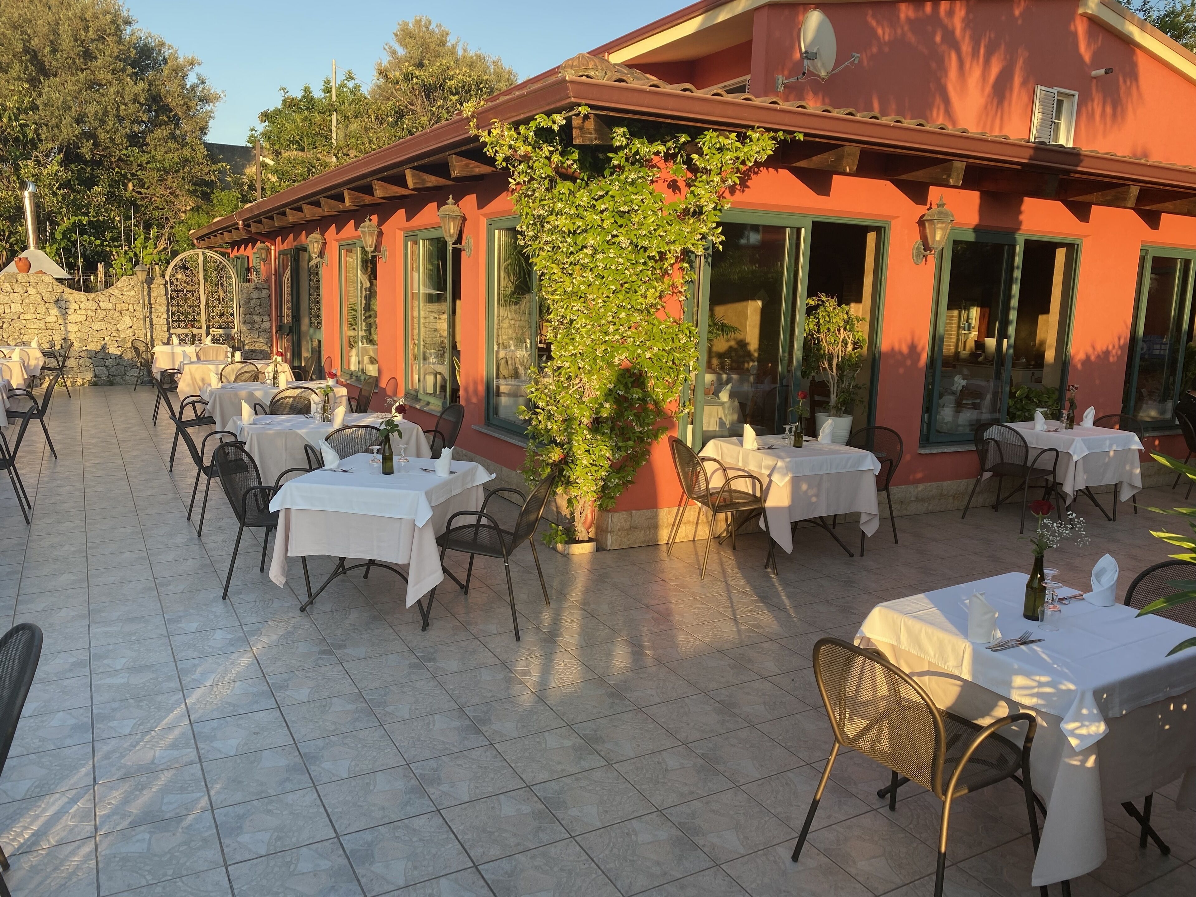 Un espace extérieur aménagé pour les repas, avec des tables pour deux personnes, entouré de murs en pierre et agrémenté de plantes en pot.