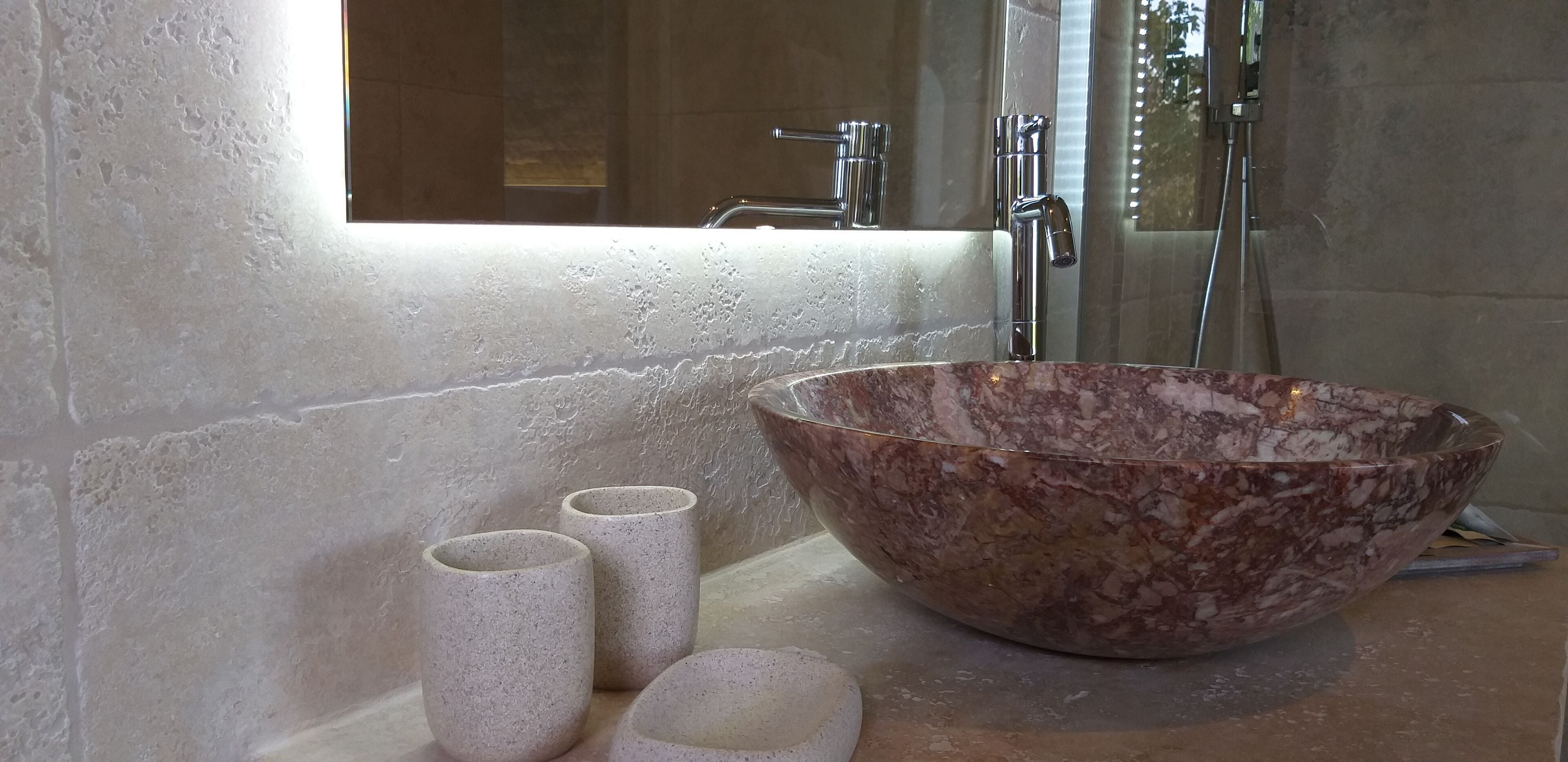 Une salle de bain avec un grand lavabo en marbre, un miroir et deux petits récipients cylindriques.