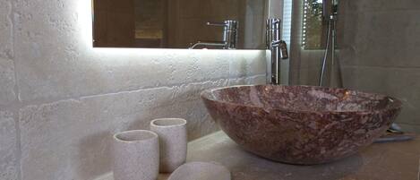 A bathroom with a large marble sink, a mirror, and two small cylindrical containers.