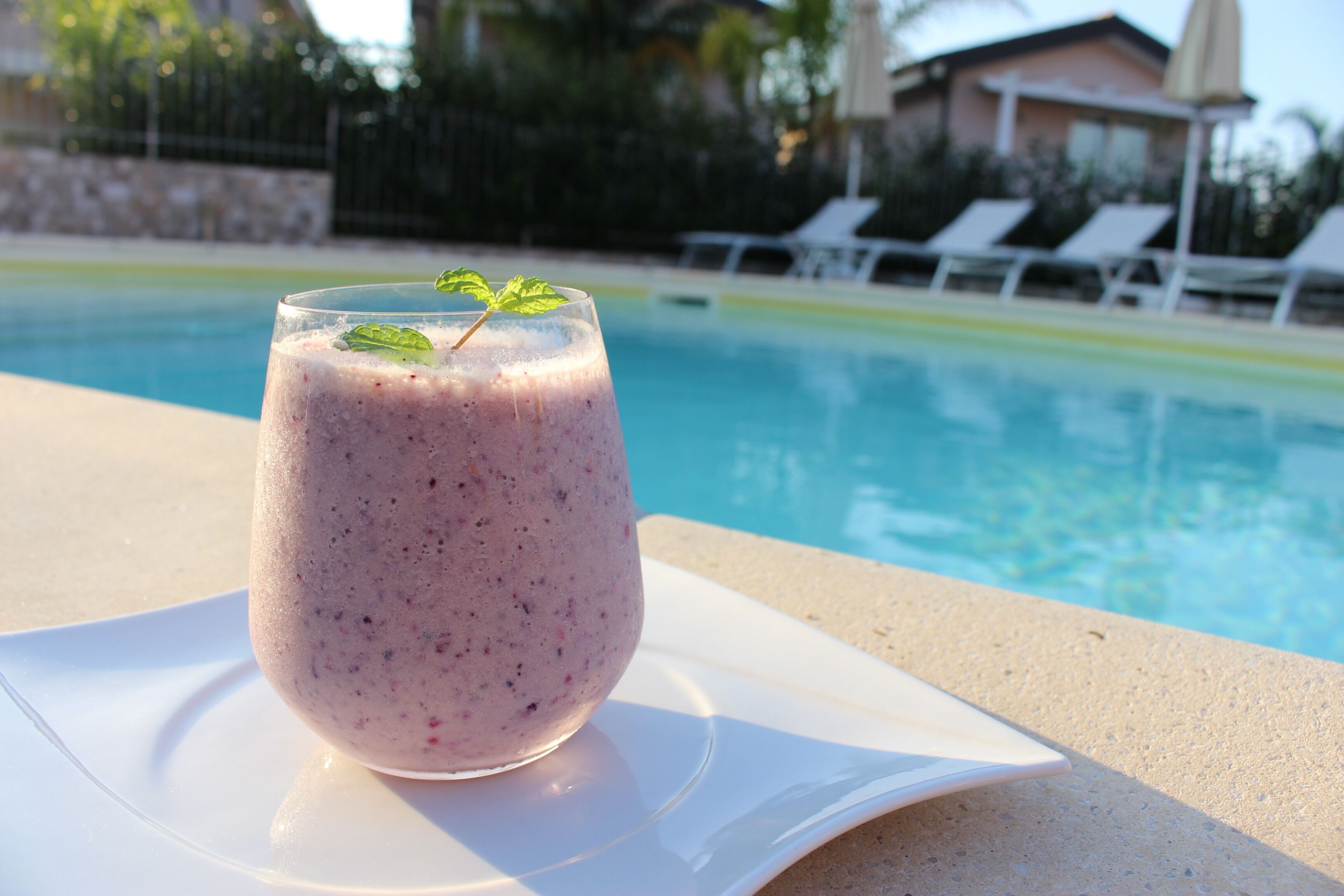 A glass of smoothie on a white plate by a poolside.