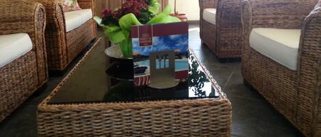 A living room with wicker furniture, a glass coffee table, and a floral arrangement.