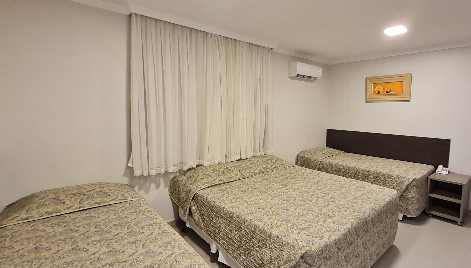 Una habitación de hotel con dos camas, una mesita de noche, un equipo de aire acondicionado y un cuadro en la pared.