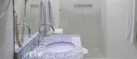 Un bagno moderno con un lavandino in granito, un asciugacapelli montato a parete e cabina doccia in vetro.