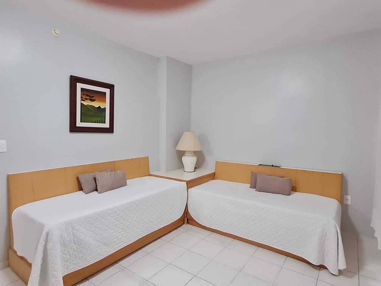 Ein Zimmer mit zwei Einzelbetten, einem Nachttisch mit Lampe und einem gerahmten Bild an der Wand.