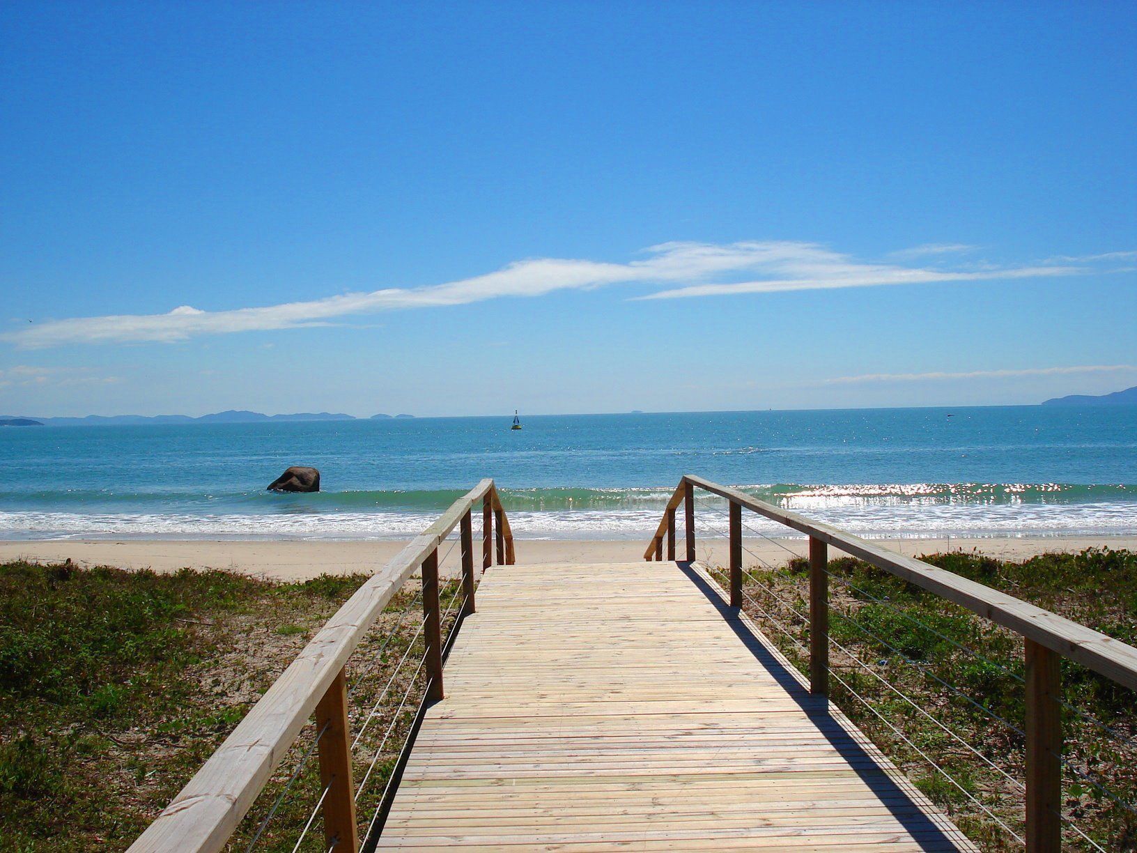 A wooden boardwalk leading to a beach with a clear view of the ocean and distant mountains.