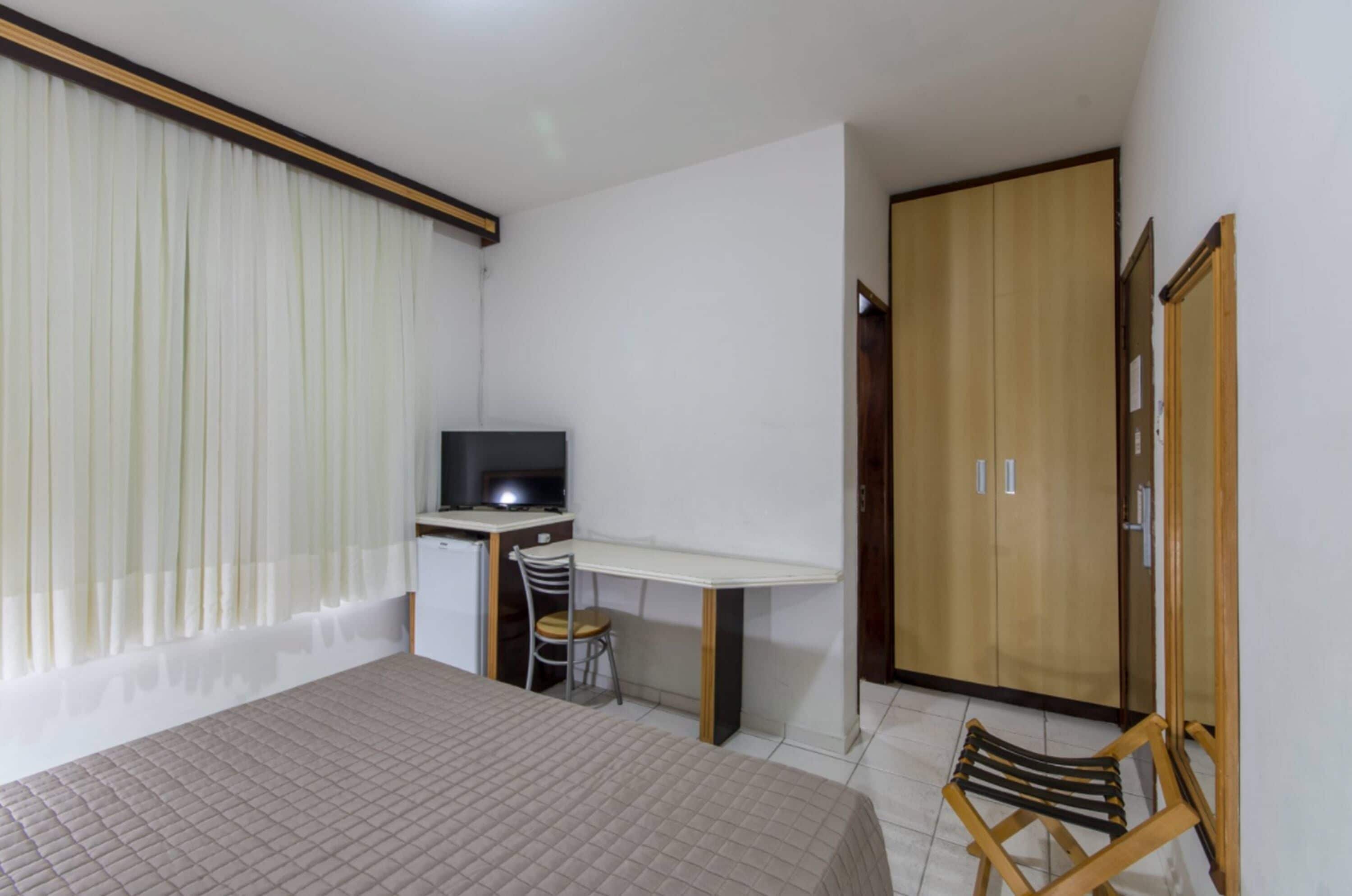 A bedroom with a bed, a desk with a chair, a television, and a wardrobe.