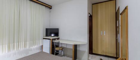 A bedroom with a bed, a desk with a chair, a television, and a wardrobe.