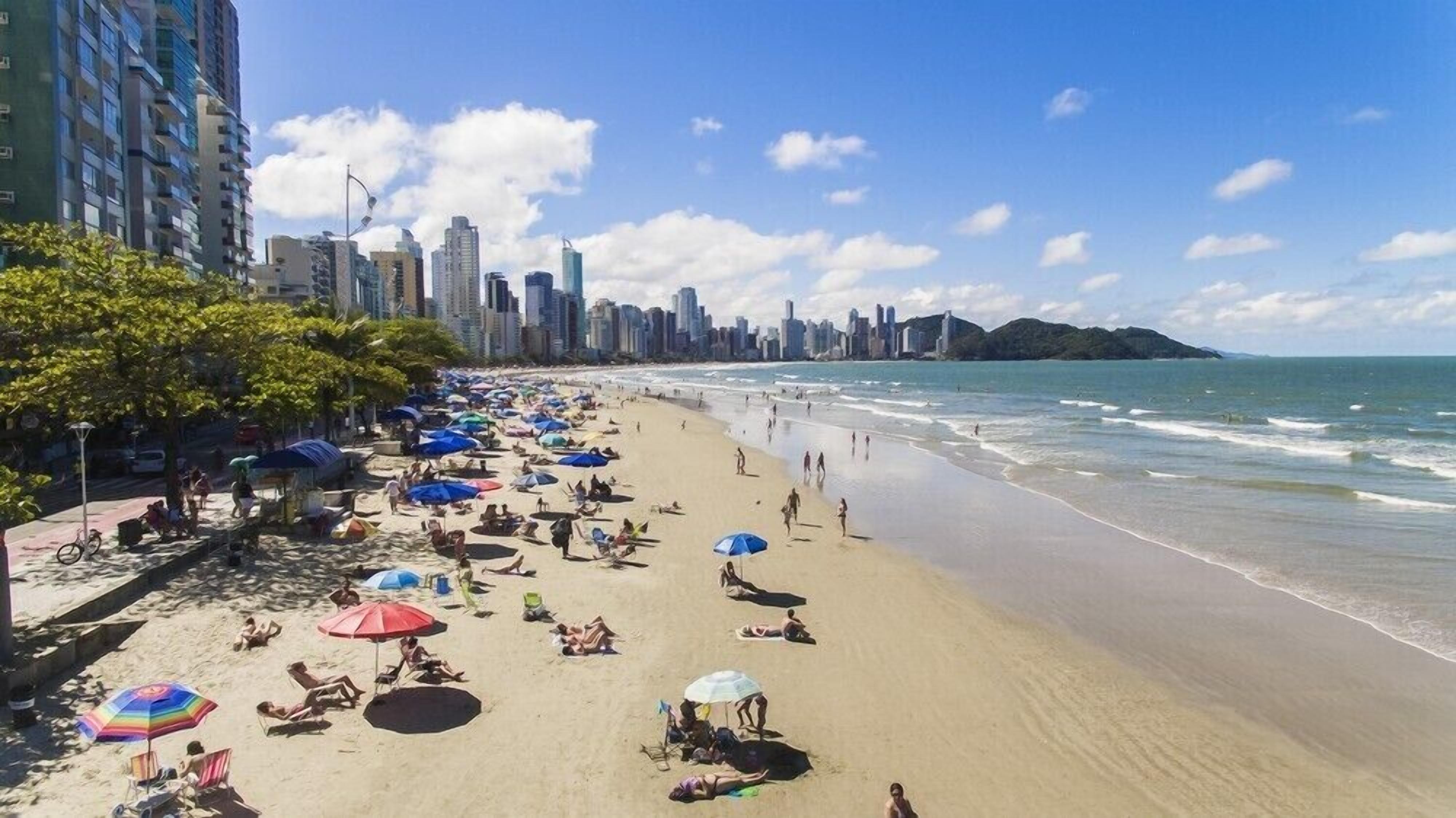 Una playa con sombrillas y gente, un horizonte urbano al fondo y un cielo despejado.