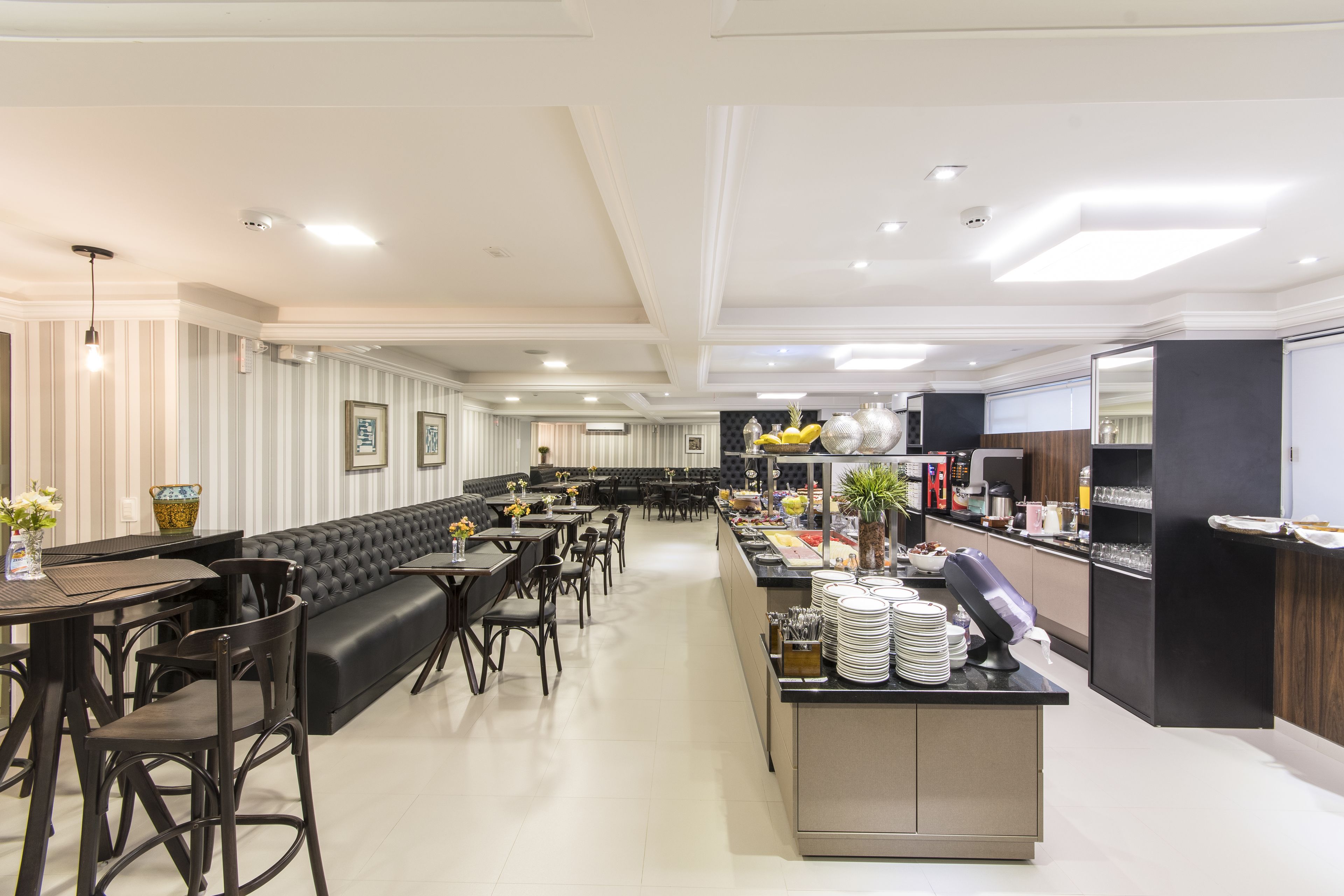 Een modern restaurant met een lange toonbank, zwarte lederen zitplaatsen en een zichtbare keuken op de achtergrond.