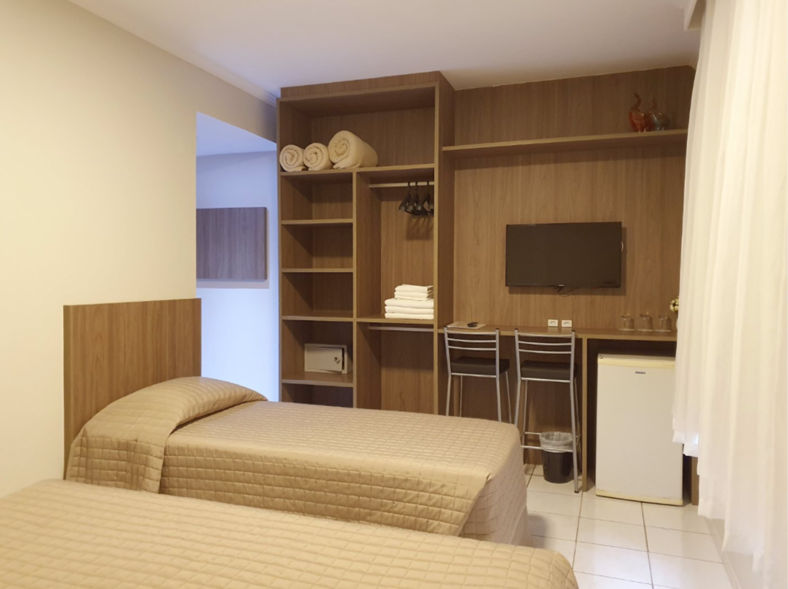 Habitación de hotel con dos camas, un escritorio, un televisor y un armario.