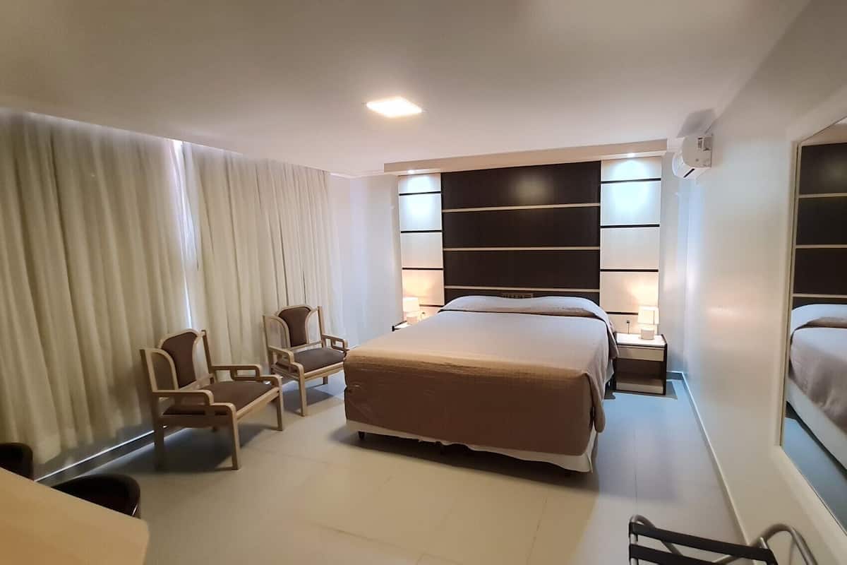 A hotel room with a large bed, two bedside tables with lamps, a chair, and a large mirror.