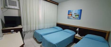 A hotel room with two single beds, a desk with a television, an air conditioning unit, and a painting on the wall.