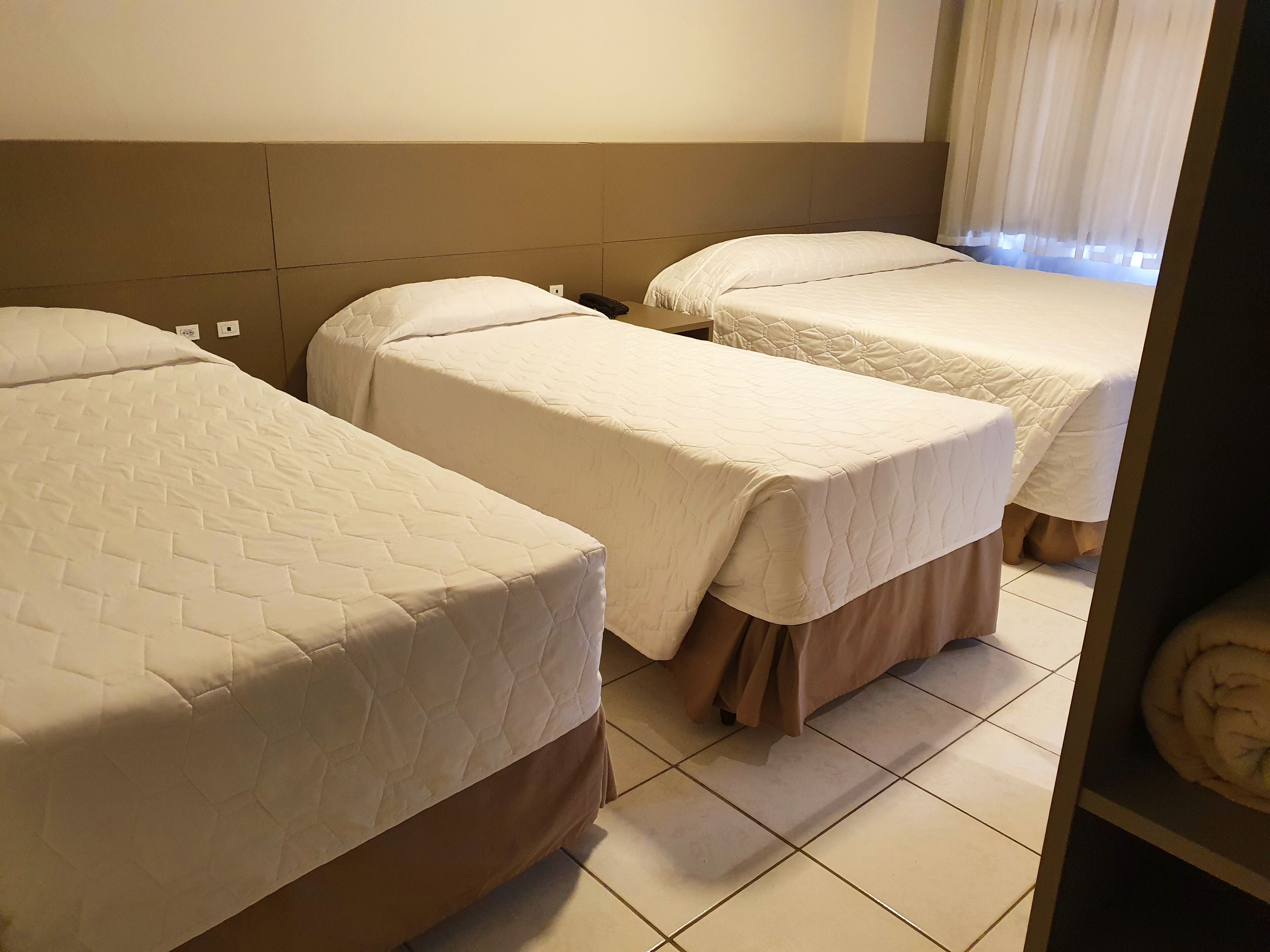 A hotel room with two beds, each with a quilted bedspread and a brown skirt at the foot.