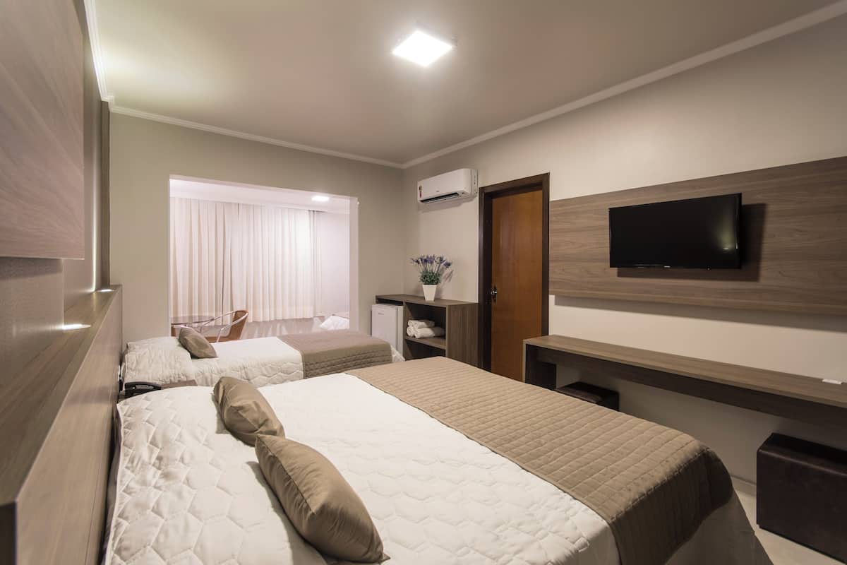 A hotel room with two beds, a TV, a desk, and a window with curtains.