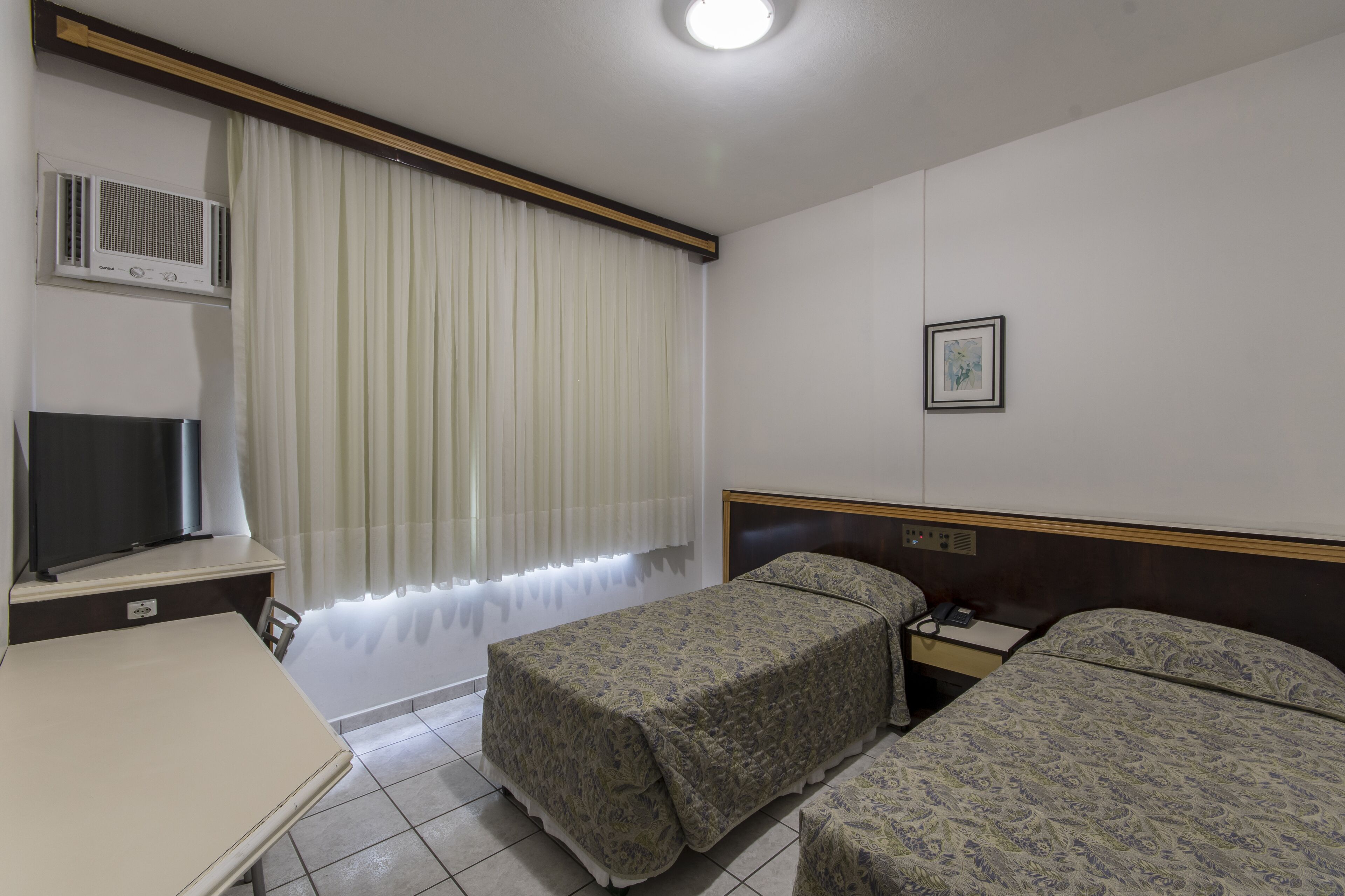 A hotel room with a bed, bedside table, TV, and a window with curtains.