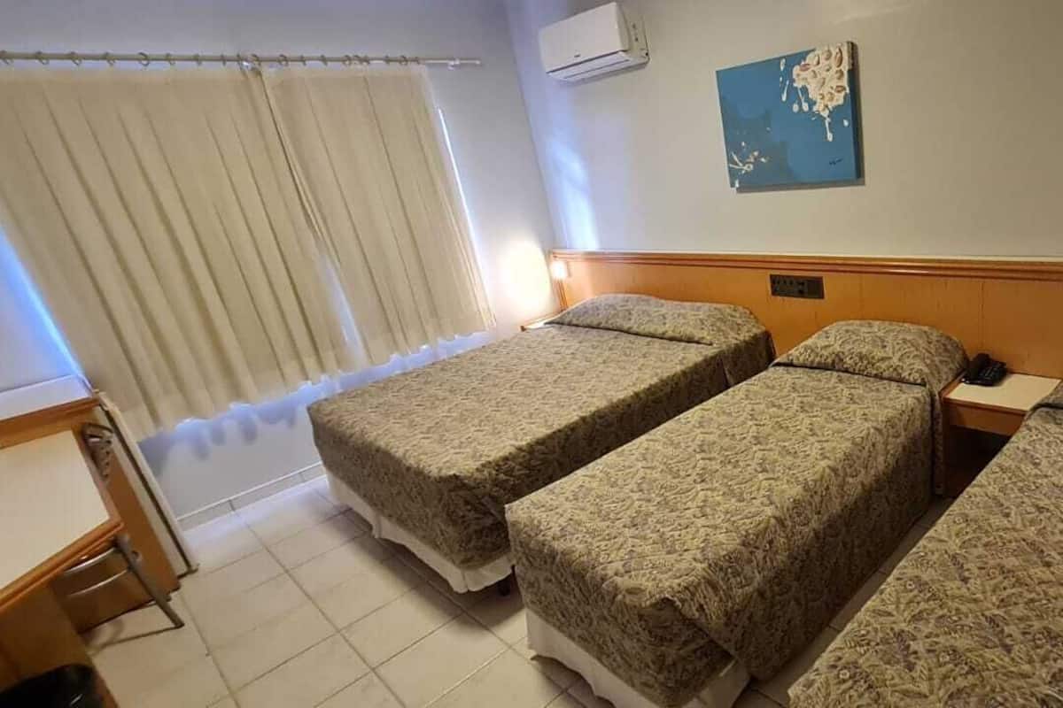 A hotel room with three beds, a desk, and a window with curtains.