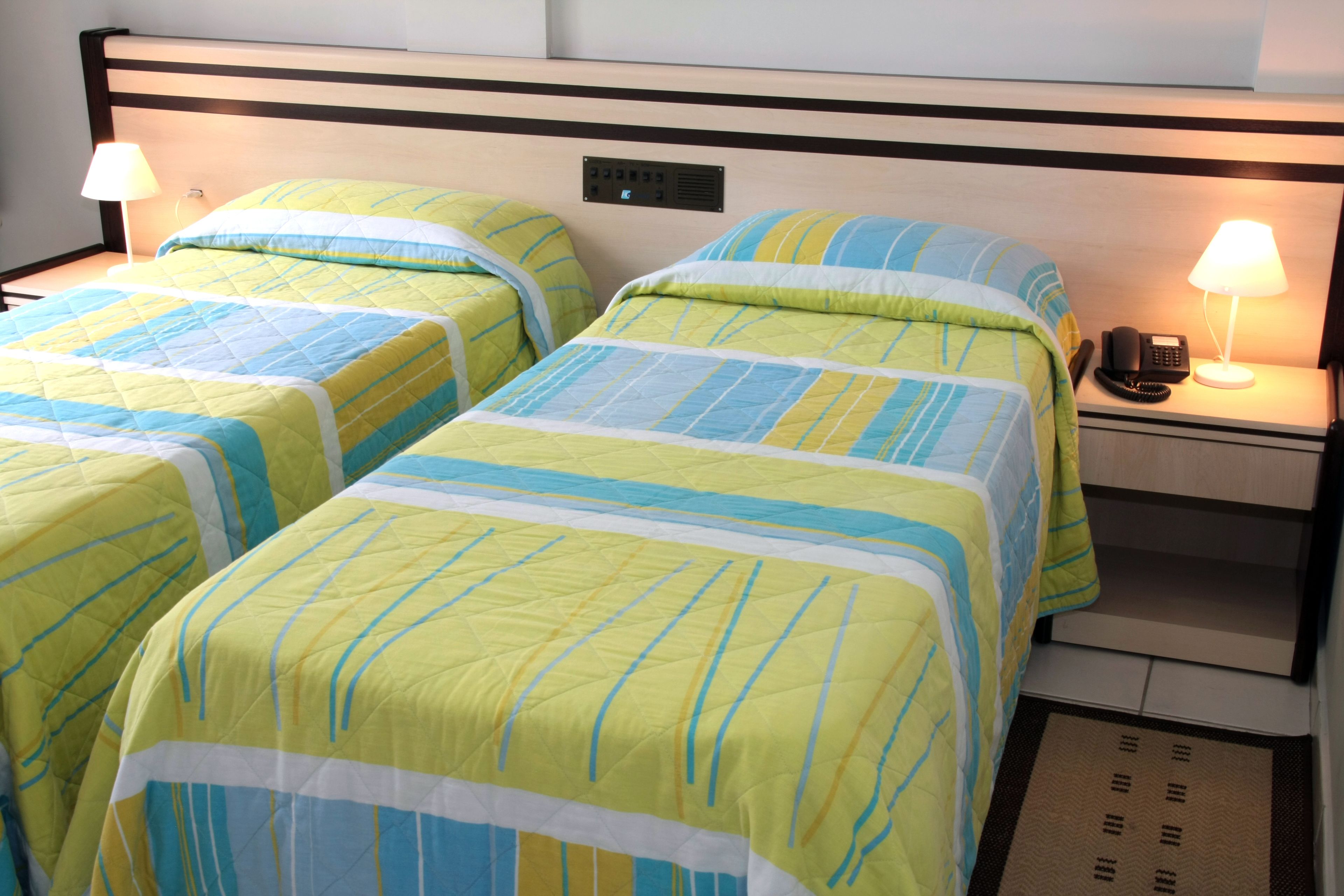 A hotel room with two beds, each with a striped bedspread, bedside lamps, and a phone on the nightstand.